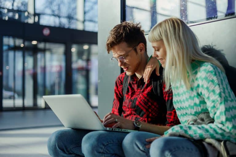 Traveling students sitting at train station and using a laptop.